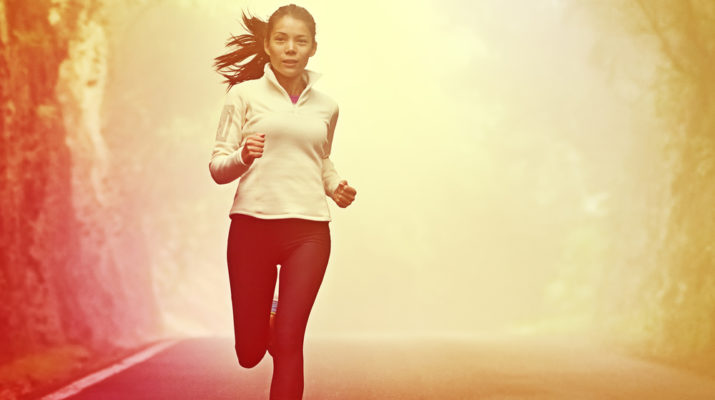 Running woman jogging on road in sunrise and mist. Female runner working out in fall or winter sports outfit. Beautiful multiracial Asian Caucasian woman athlete outside.